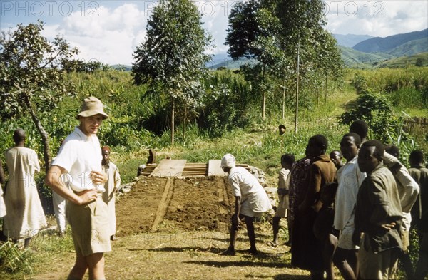 Bridge-building in Toro'. An ADC oversees a community development project to build a new bridge. According to an original caption, the local community provided timber and unpaid labour for the project. Toro, West Uganda, June 1957., Central (Uganda), Uganda, Eastern Africa, Africa.