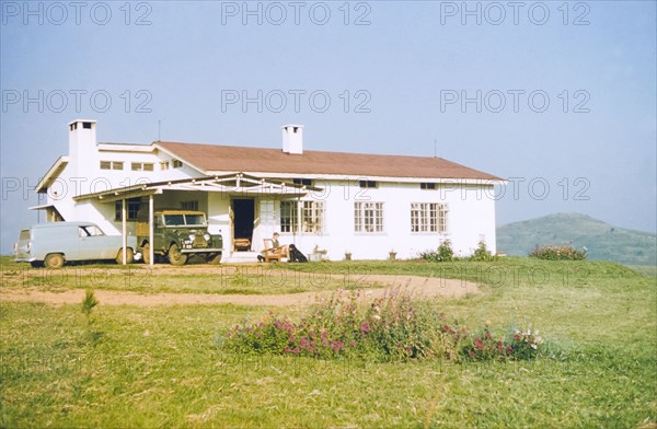 Bungalow in Fort Portal. District Forestry Officer James Lang Brown sits reading in an armchair outside his new bungalow in Fort Portal. An original caption comments that the bungalow was shared with David Pasteur, an Assistant District Commssioner. Fort Portal, West Uganda, 1957., West (Uganda), Uganda, Eastern Africa, Africa.