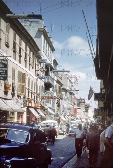 A street in Gibraltar'. View along a city street in Gibraltar, bustling with traffic, pedestrians and street signs. Gibraltar, July 1958. Gibraltar, Gibraltar, Gibraltar, Mediterranean, Europe .