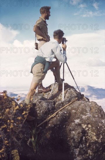 On the summit of Mount Napak. District Forestry Officer James Lang Brown (left) surveys Karamoja from the summit of Mount Napak. With him, crouched behind a camera and tripod, is Assistant District Commisioner John Cleeve. North East Uganda, December 1958., East (Uganda), Uganda, Eastern Africa, Africa.