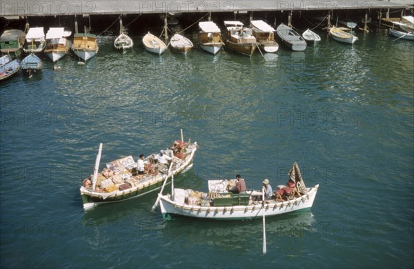 Bumboats at Port Said'. Two bumboats filled with trade wares float in the harbour at Port Said. Several smaller boats are moored to a jetty nearby. Port Said, Egypt, 1958. Port Said, Port Said, Egypt, Northern Africa, Africa.