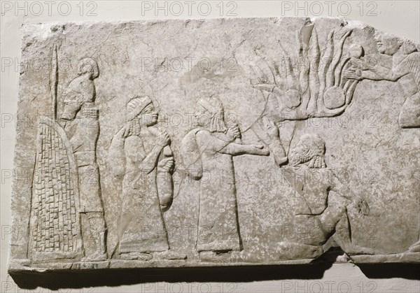 Stone relief depicting Babylonian and Chaldean prisoners in camp, under guard, with a log fire burning behind