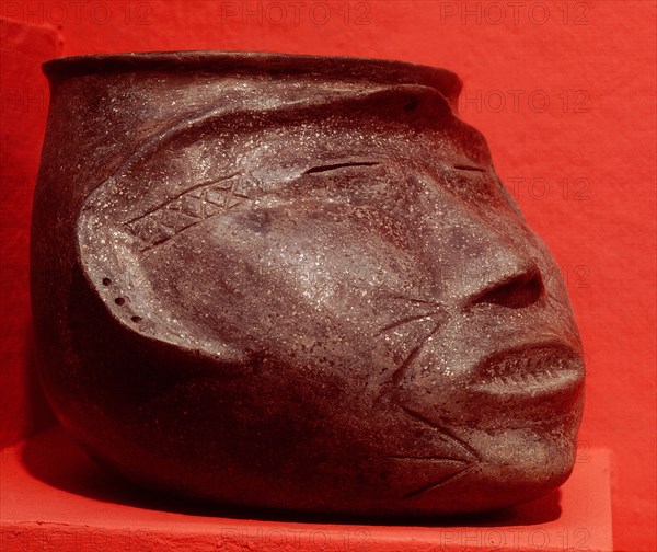 Pottery effigy head vessel representing a trophy head with sealed eyes and mouth sewed shut