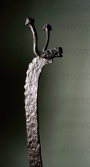 Detail of the upper end of a wrought iron fire dog in the shape of a stylized bovine animal with balled horns