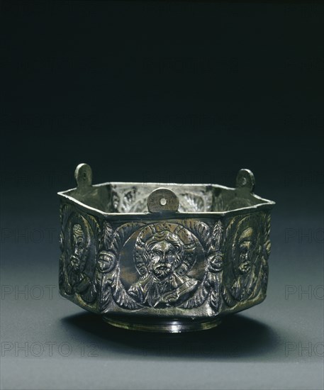 A six sided silver vessel on each side of which is a roundel containing a bust of Christ, the Virgin, Peter, Paul, John and James