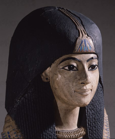 A mummy mask of a man wearing an elaborate collar and a heavy wig adorned with a lotus blossom