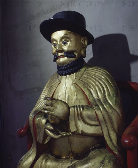 A gilt statue of Marco Polo holding a pomegranate, symbol of wealth and prosperity