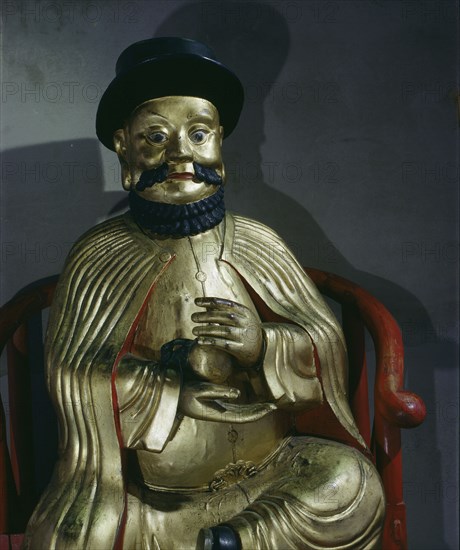 A gilt statue of Marco Polo holding a pomegranate, symbol of wealth and prosperity