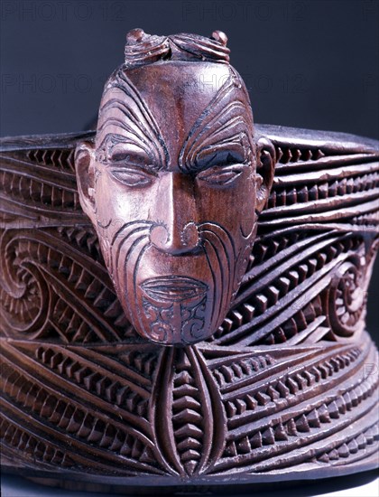 A oval lidded wooden box with scrolled carvings on the sides and a male and female head carved at the ends