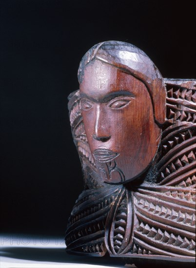 A oval lidded wooden box with scrolled carvings on the sides and a male and female head carved at the ends