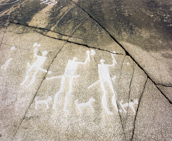 Petroglyph with three men brandishing axes, accompanied by dogs