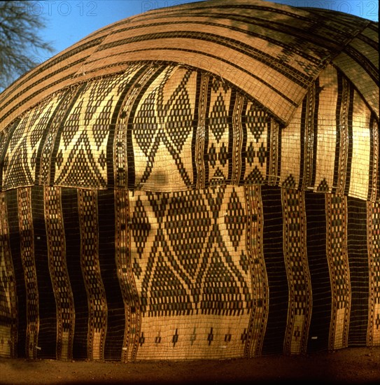 A tent walled with woven fibre mats, elaborately decorated for special occasions