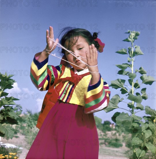 A young Korean girl in traditional dress playing Cat's Cradle
