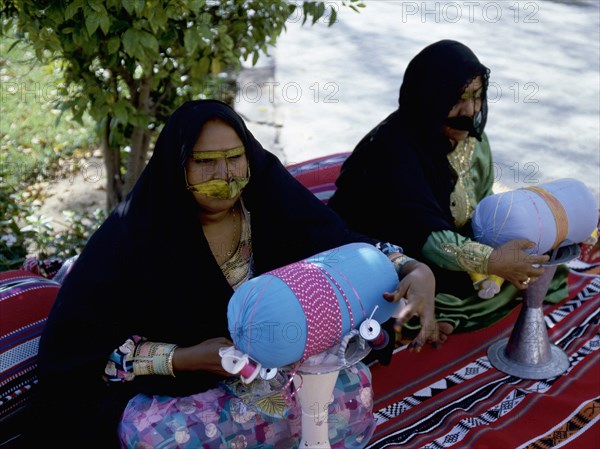 Two women wearing black veils and burqa face masks prepare coloured braids