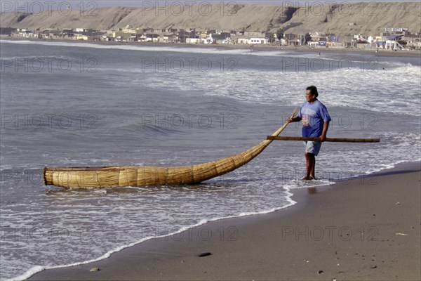 Modern day Moche fisherman guiding a tortora reed boat (caballito) on beach on Peru's northern coast