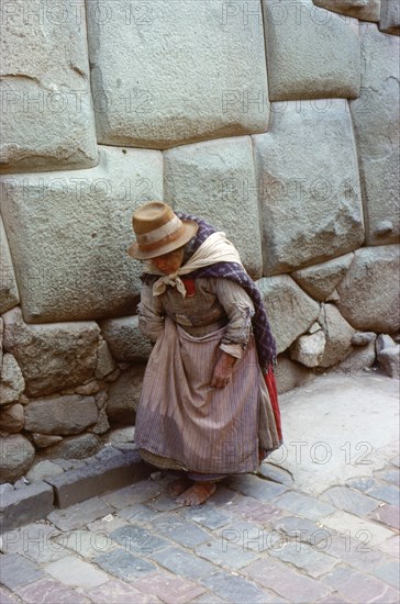 Quechua (Inca) woman in Colonial-period dress walking past typical Inca Masonry in the famous Inca Street of Hatun Rumiyoc, Cuzco