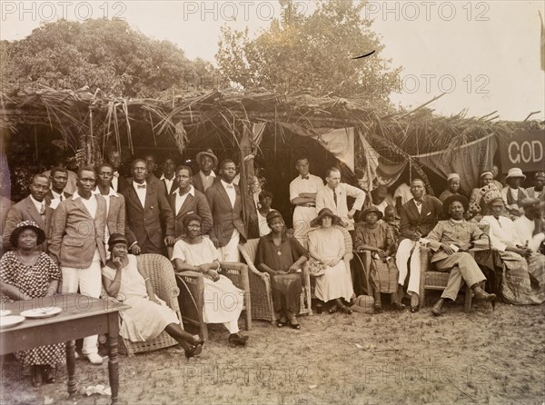 Group standing and seated under palm frond awnings