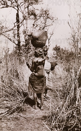 Sudanese women walking with a child on her back and a pot on her head