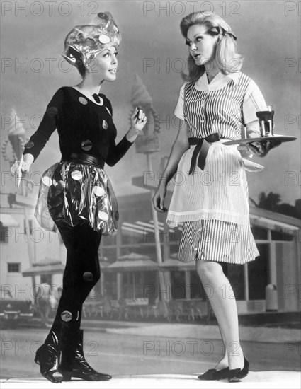 Cleveland, Ohio: March 20, 1967.
The Work Wear Corp. has created uniforms for carhops of the present and the future. The present is wearing a red and white striped cotton dress, and the carhop of the future wears a black leotard with an accesorized clear vinyl skirt