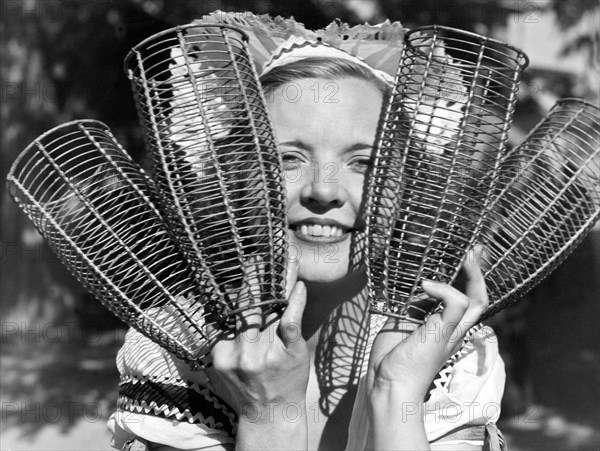 California:  c. 1934.
A woman holding up the baskets that will dress the California champagne bottles at the first wine festival to be held since Prohibition.