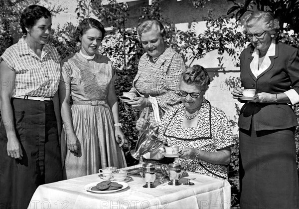 California:   c. 1948.
Four women gather around a table outdoors while another one serves coffee and cookies.