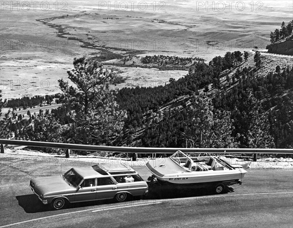 A station wagon towing a power boat heads up into the mountains