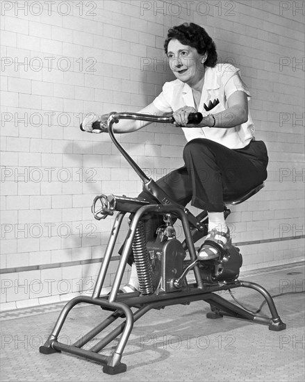 United States: c. 1960.
An older woman pedals on her exercycle.