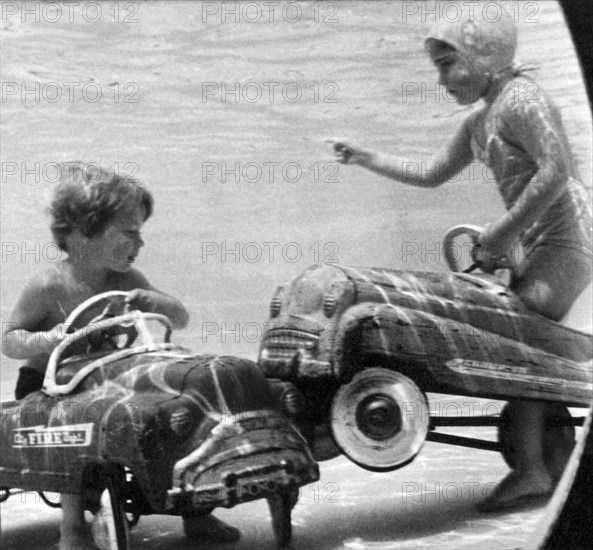 United States:  c. 1958.
Two children move their playground toys into the pool, where accidents are bound to happen.