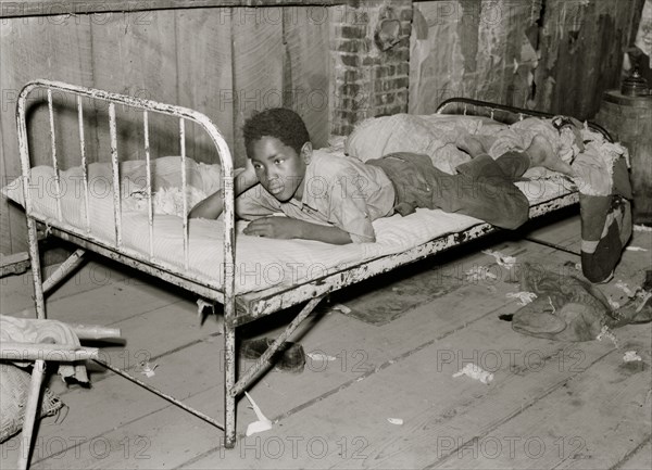 African American Boy resting on bed in attic of sharecropper shack. New Madrid County, Missouri 1938