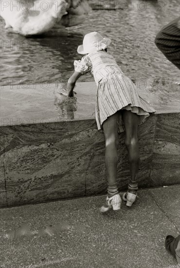 African American Girl leans over fountain pool to play with water 1939