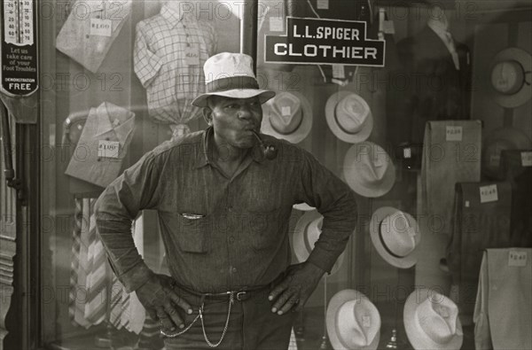 African American Resident of Plain City, Ohio smoking a pipe outside of a clothing store 1935