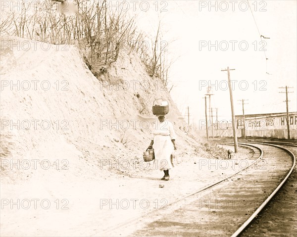 African American woman with basket on head walking near railroad tracks 1921