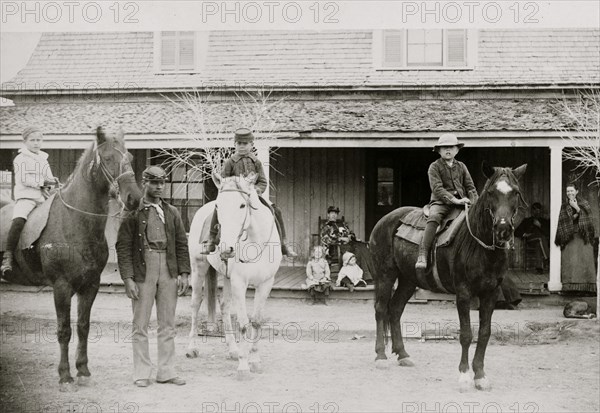 Afro-American enlisted man standing by three officers' children on horseback, Fort Verde, Arizona 1886