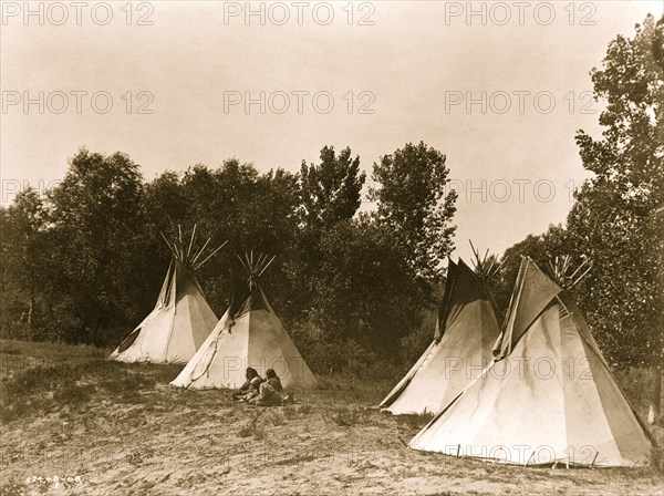 An Assiniboine camp containing four tepees with Indians seated on ground 1908