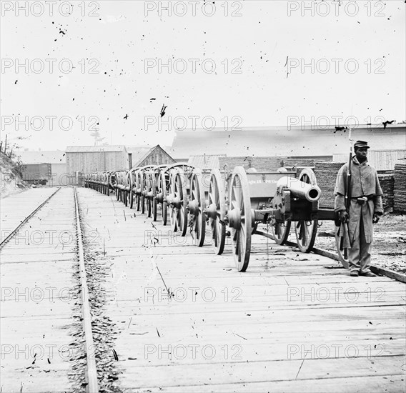 Black soldier guarding a line of 12-Pound Napoleons; Artillery Mounted on Caissons 1864