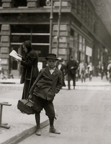 Bundle Boy carry packages in back a woman on crutches reads a newspaper. 1910
