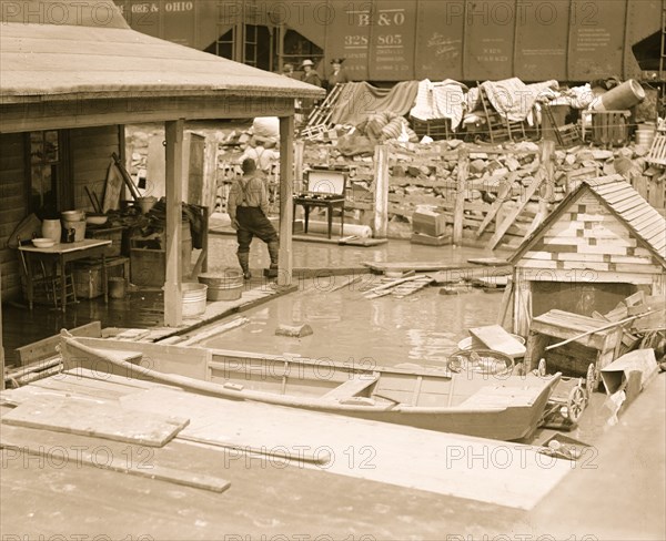 Canoes abound as flood waters lap the shore under  concrete bridge and beside railroad hopper cars. 1924