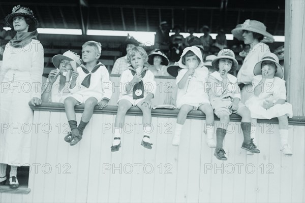 Children sit on wall in front of stands at the ballpark and eat ice cream cones.