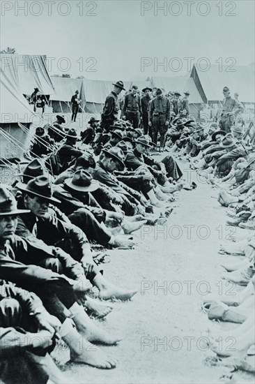 Foot Inspection, soldiers sit on ground while doctors prepare to examine a full unit at once 1917