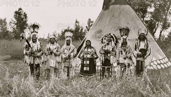 Group of Siksika (Blackfeet) men and one woman singing in front of tipi 1913