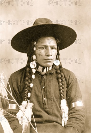 Portrait of Indian with decorated face, feather and bead ornaments, 1903