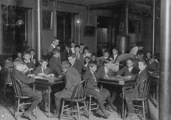 In the Newsboys Reading Room. Boys seated at tables playing gamers. 1909