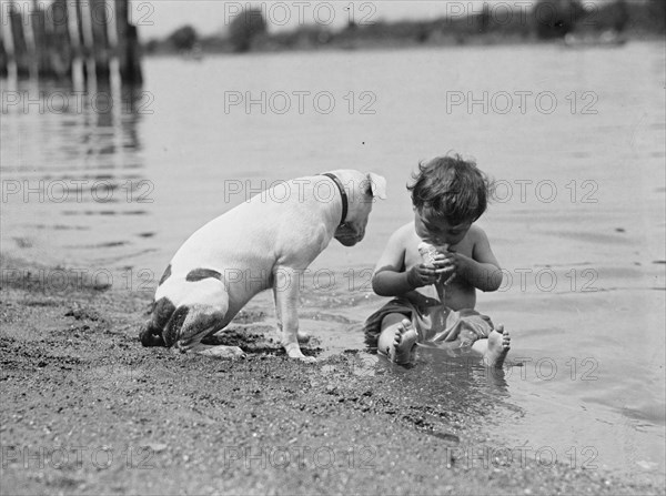 Inquisitive Baby sits in sand at beach and tucks his head into an ice cream cone 1925