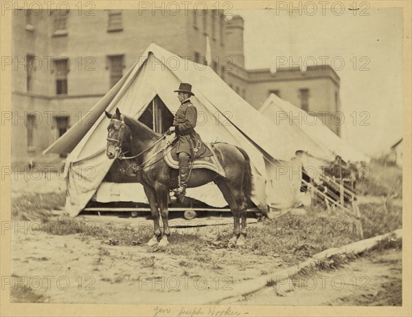 Major-General Joseph Hooker, full-length portrait, seated on horse, facing left, wearing military uniform, two tents and large building in the background 1863