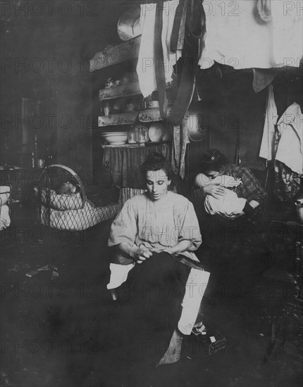 Mrs. Tony Racioppo, 260 Elizabeth St., N.Y. 1st floor rear, finishing pants in dirty tenement home. Although] it is a licensed house, the whole place is very much run down. The hallway [i.e., hallway] is in the same condition as that one at 266 Elizabeth (see photo). Baby had bad cough. Mother said recovering from measles 1912