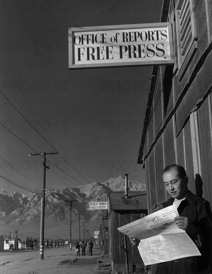 Roy Takeno reading paper in front of office 1943