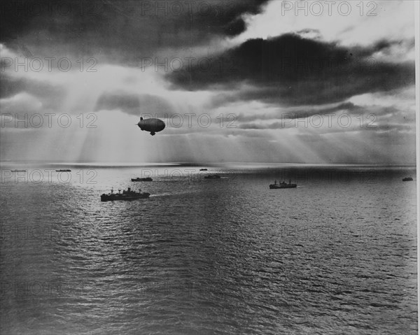 Sunset over the Atlantic finds another United Nations convoy moving peacefully towards it destination. A U.S. Navy blimp, hovering watchfully overhead, is on the lookout for any sign of enemy submarines 1943