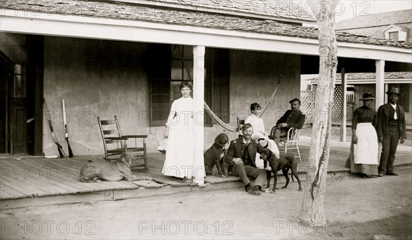 Two soldiers and two women on porch, with Afro-American woman and man to right, Fort Verde, Arizona 1886