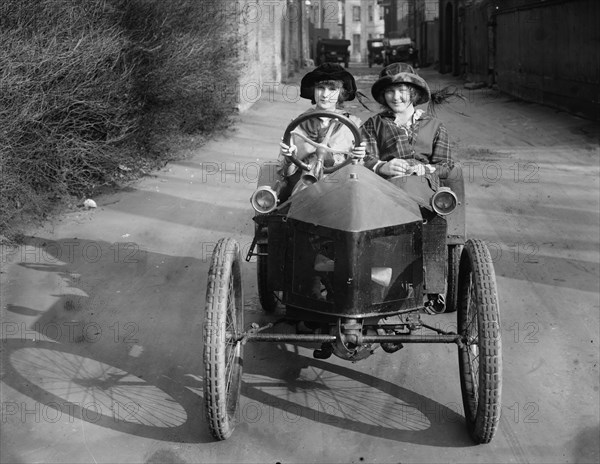 Two Teenage Girls; one takes the wheel of a less than full-sized car