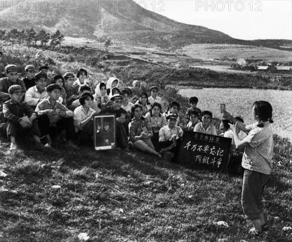 During a work break, a young woman is leading the commune workers in singing a song praising chairman mao, cultural revolution, tachai, shansi province, china, 1968.